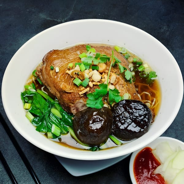 Vietnamese duck noodle soup with bok choy, mushrooms, and scallions, served with chili sauce and pickled onions.