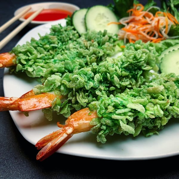 Two green crispy shrimp with tails, served with sliced cucumbers, shredded carrots, and dipping sauce.