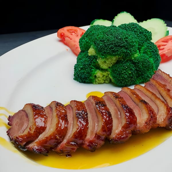 Sliced roasted duck with a glossy skin, served with broccoli, tomato, and cucumber on a white plate.