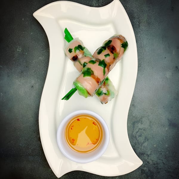 Two Vietnamese spring rolls with green onions and meat, served with a dipping sauce.