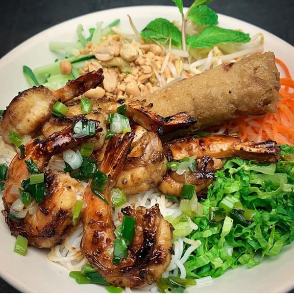 Vietnamese vermicelli bowl with grilled shrimp, spring roll, peanuts, mint, and fresh vegetables.