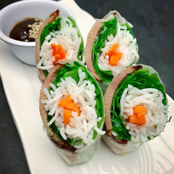 Four Vietnamese spring rolls with beef, lettuce, rice noodles, and carrots, with dipping sauce.
