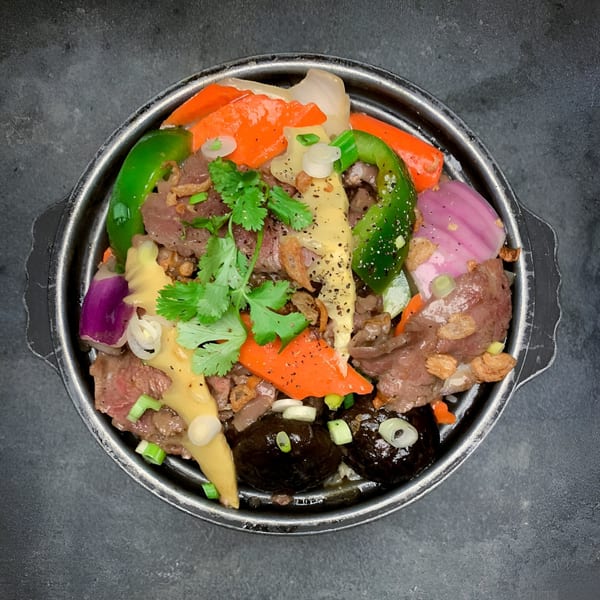 Vietnamese beef stir-fry with colorful vegetables, mushrooms, and herbs in a metal bowl.
