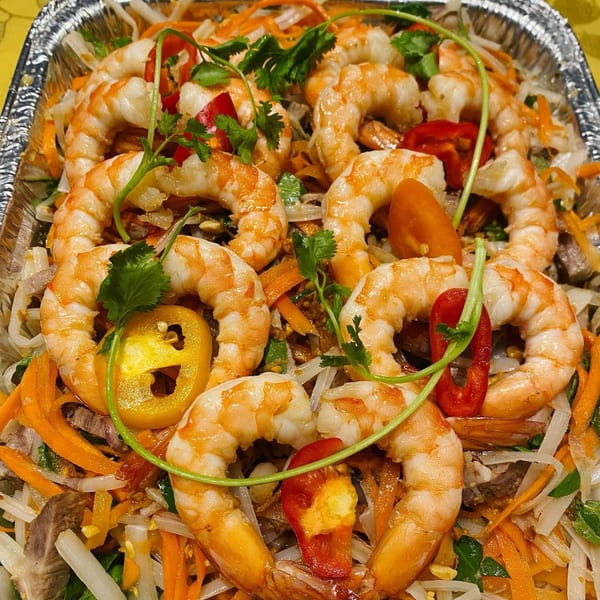 Vietnamese shrimp salad with noodles, carrots, bell peppers, and cilantro in a foil container.