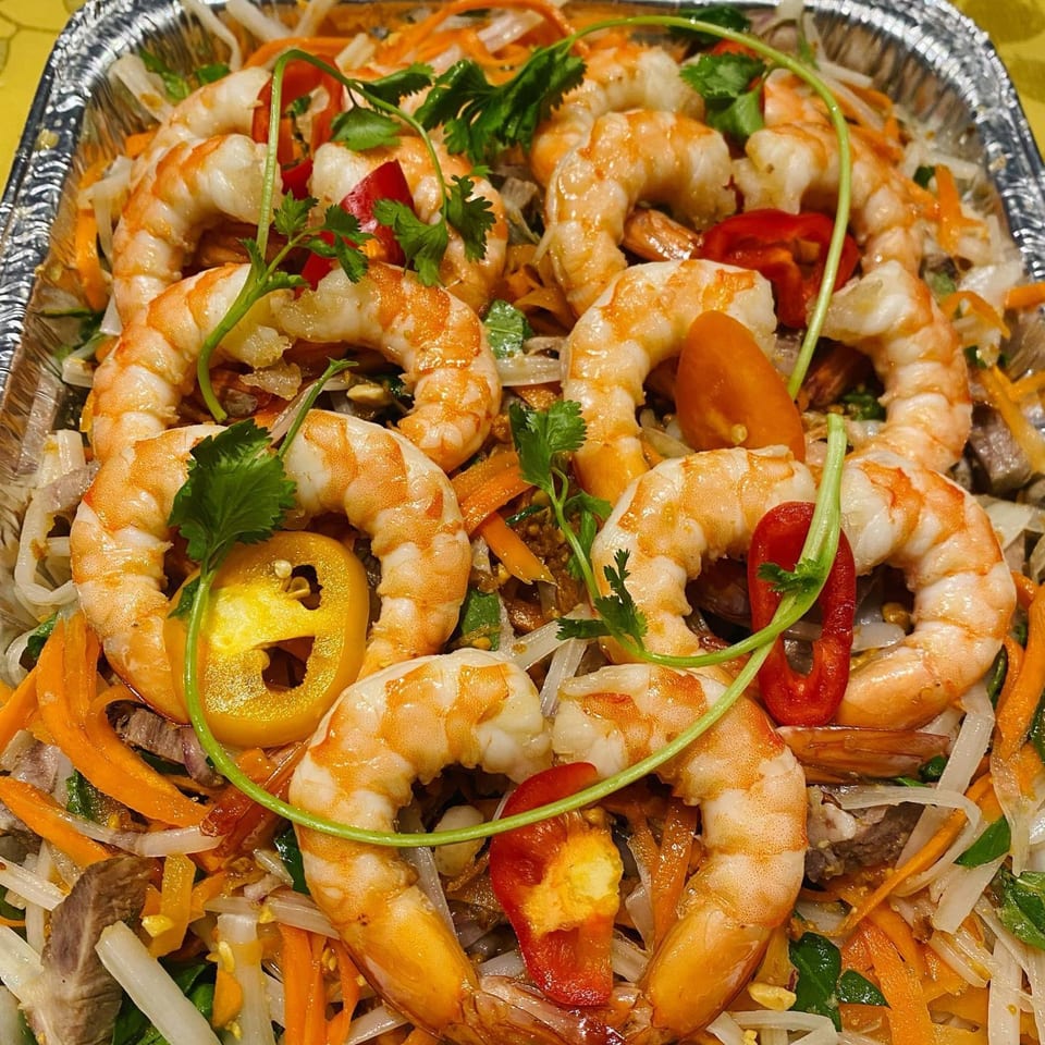 Vietnamese shrimp salad with noodles, carrots, bell peppers, and cilantro in a foil container.